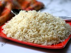 a red plate topped with rice on top of a table next to a fork and napkin