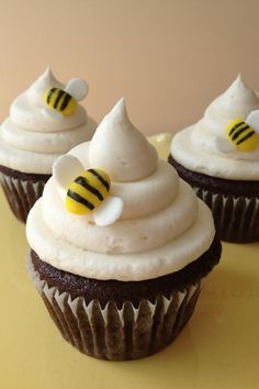 three cupcakes with white frosting and honeybee decorations on top are sitting on a table