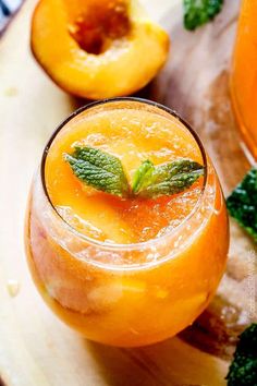 an orange drink with mint garnish in a glass next to two peaches