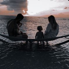 a woman and two children sitting in a boat on the water at sunset or dawn