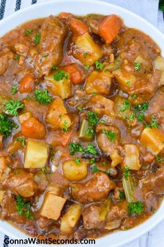 a white bowl filled with stew and vegetables on top of a table cloth next to a spoon