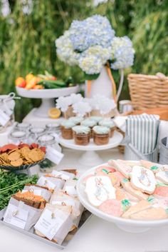 a table filled with desserts and cookies on top of white tables covered in greenery