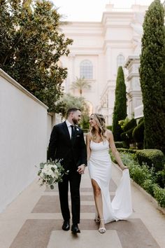 a bride and groom walking down the sidewalk holding hands