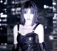 a woman with black hair and leather outfit posing in front of a cityscape