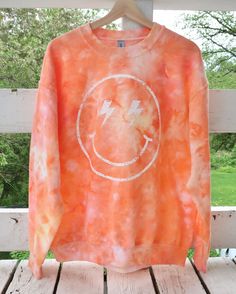 an orange and white tie - dye shirt with a smiley face on the front, sitting on a porch