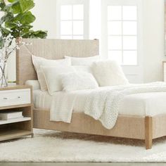 a bed with white linens and pillows in a room next to a plant on a table