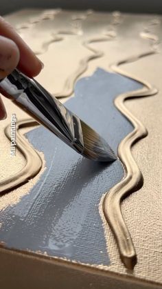 a person is using a brush to paint a piece of art with metallic foil on it