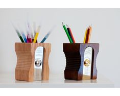 two wooden pencil holders sitting on top of a white counter with pens and pencils in them