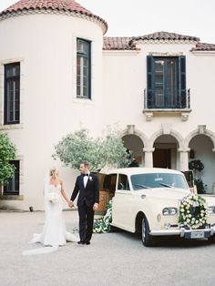 a bride and groom walking towards their wedding car in front of a large white building