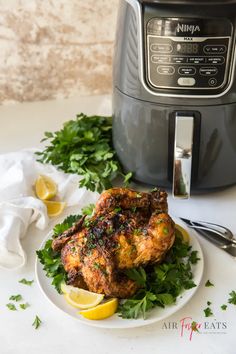 a white plate topped with chicken next to an air fryer and lemon wedges