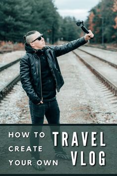 a man in black jacket and sunglasses holding an umbrella over his head while standing on train tracks