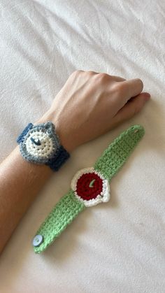 two crocheted wristbands on top of a bed with a person's hand