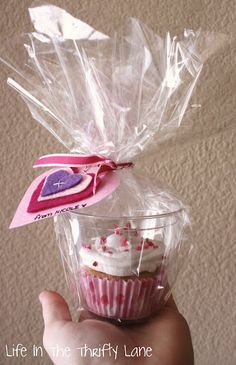 a hand holding a cupcake wrapped in plastic