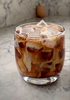 an iced drink in a glass with ice cubes on the rim, sitting on a marble countertop