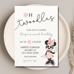 a pink and black minnie mouse birthday party card on a white plate next to some dried flowers