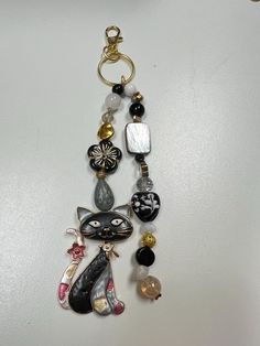 a cat keychain hanging from a hook on a white surface with beads and charms