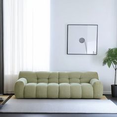 a living room with a green couch and potted plant on the floor next to it