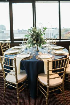 the table is set with white and blue linens for an elegant wedding reception in front of large windows