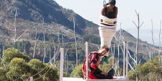 two people are hanging upside down in the air on a rope bridge with trees and mountains in the background