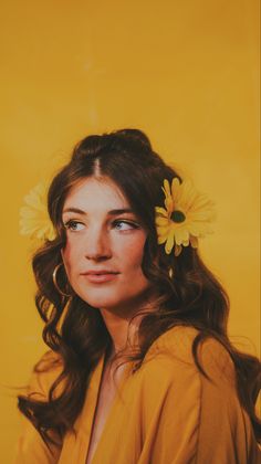 a woman with flowers in her hair is posing for a photo against a yellow background