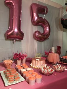 a pink table topped with lots of cupcakes and cake