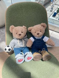 two teddy bears sitting on a green chair with soccer balls and shoes next to them