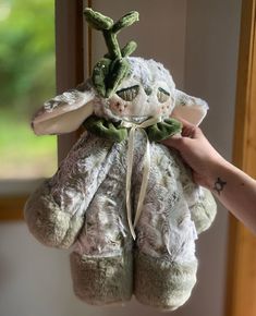 a stuffed animal is being held up by a person's hand in front of a window