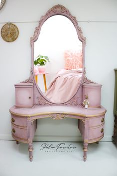 a pink dressing table with a mirror on it and a plant in the corner next to it