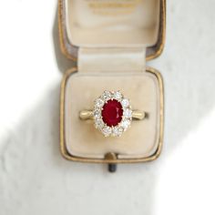 an engagement ring with a red stone surrounded by white diamonds in a velvet presentation box