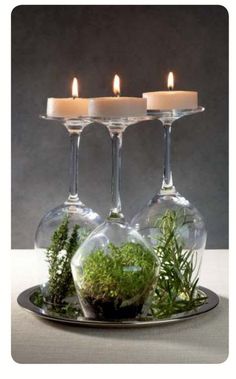 three wine glasses filled with moss and lit candles on a plate next to each other