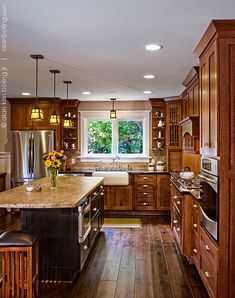 a large kitchen with wooden cabinets and an island in the middle is lit by two pendant lights