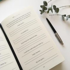 an open notebook sitting on top of a table next to a pen and some flowers