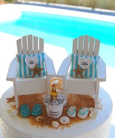 two beach themed chairs sitting on top of a table next to a pool and sand