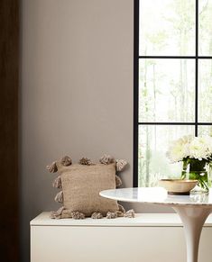 a vase with flowers sitting on top of a white table next to a large window