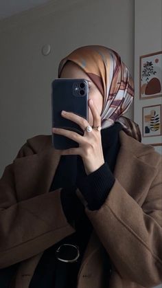 a woman wearing a headscarf taking a selfie with her phone