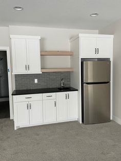 an empty kitchen with white cabinets and black counter tops, including a refrigerator freezer