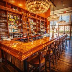 a bar with wooden shelves and stools next to a chandelier hanging from the ceiling