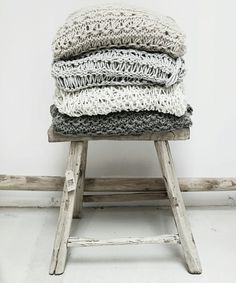 four blankets stacked on top of each other in front of a white wall and wooden stool