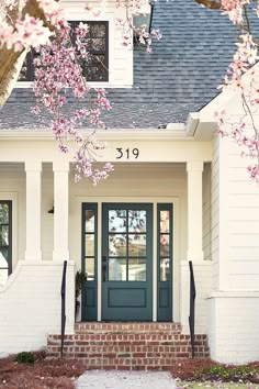 a white house with blue front door and pink flowers on the tree in front of it