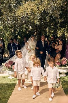 three children are walking down the aisle with their parents and wedding party in the background