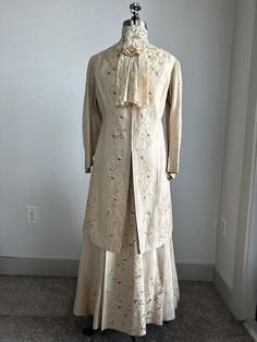 1800s Edwardian Era 3-Piece Daisy Chained Embroidered Light Gold Silk Wedding or Day Suit Dress Measures: Dickie: Neckline:15" Jacket: Bust:  40" Waist:  35" Hip: 42" Shoulder to Shoulder:15" Shoulder to Sleeve Hem:21" Shoulder to Front Hem:40" Shoulder to Back Hem:40" Skirt: Waist:26" Hip: 48" Waist to Hem Front: 38" Waist to Hem Back: 40" Details: -3-Piece Set Includes: Dickie, Jacket and Skirt -Irish Lace, High Collar, Dickie with Front Bow and Tails with Snap Back Closure -Light Gold, Heavy Linen Jacket Bodice with Daisy-Chain, Cotton Embroidery of Light Gold, Gold, and Ecru -Collarless Jacket with Straight Paneled Front with Hook and Eye Closure, Long sSleeves and 3/4 Length Hem -Jacket Embroidered Down Front Closure Panels, Back Yoke, Sleeve Shoulders, Cuffs and Hemline  -Jacket is F Formal Gold Raw Silk Dress, Gold Raw Silk Dress For Formal Occasions, Elegant Victorian Brocade Dress For Costume, Elegant Brocade Victorian Dress For Costume, Elegant Embroidered Gown For Transitional Season, Elegant Victorian Brocade Dress With Historical Design, Elegant Ceremonial Gown With Intricate Embroidery, Vintage Brocade Victorian Dress For Costume, Traditional Wedding Dress With Historical Design