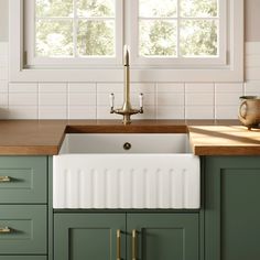 a kitchen with green cabinets and white tile on the walls, an apron style sink in front of a window