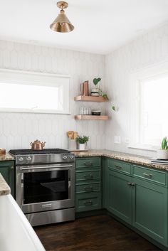 a kitchen with green cabinets and stainless steel stove top oven in the center, surrounded by wooden shelves