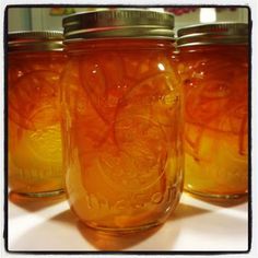 three jars filled with orange liquid sitting on top of a white countertop next to each other