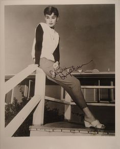 an old black and white photo of a woman sitting on a railing