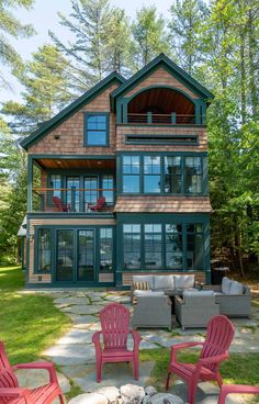 two red chairs sitting on top of a stone patio next to a wooden house with large windows