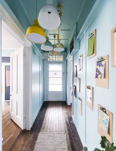 a long hallway with blue walls and pictures on the wall, along with hanging lights