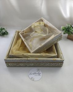 an open box with a yellow ribbon in it on a white surface next to some plants