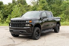 a black truck is parked in a parking lot with trees in the backgroud