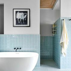 a white bath tub sitting next to a blue tiled wall in a bathroom under a painting